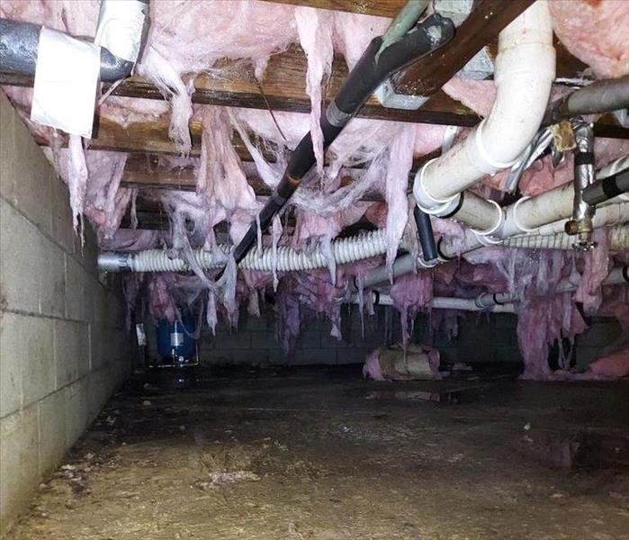 Crawlspace with hanging and wet insulation above dirt substrate